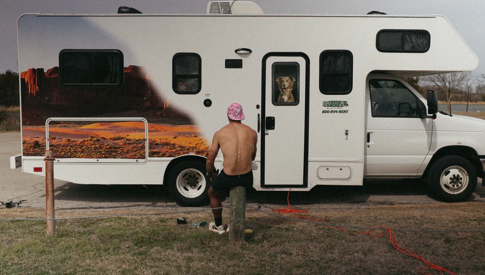 Lachlan beside the camper, with a dog looking through its door window.